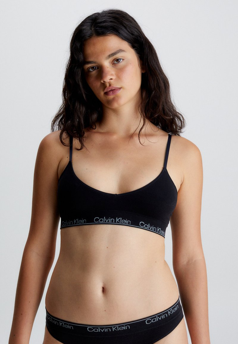 Czarny stanik braletka z regulowanymi ramiączkami, z szerokim elastycznym pasem z logo "Calvin Klein" w kontrastowym kolorze. Gładki, minimalistyczny design.