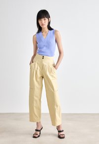 Haut sans manches en ribbed bleu clair avec décolleté en V, associé à un pantalon large crème avec deux poches avant et des accents de boutons noirs.