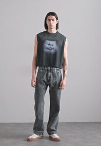 Black cropped sleeveless shirt with a graphic design of a cat's face, paired with gray distressed jeans and white sneakers with brown soles.