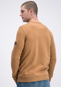 Brązowa bawełniana bluza z okrągłym dekoltem, ściągaczami przy mankietach i dole. Mała naszywka z logo na lewym rękawie. Gładka struktura, luźny krój.