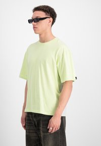Camiseta de gran tamaño en verde claro, hecha de tela suave, con mangas cortas y escote redondo. Combinada con pantalones de mezclilla oscuros y gafas de sol.