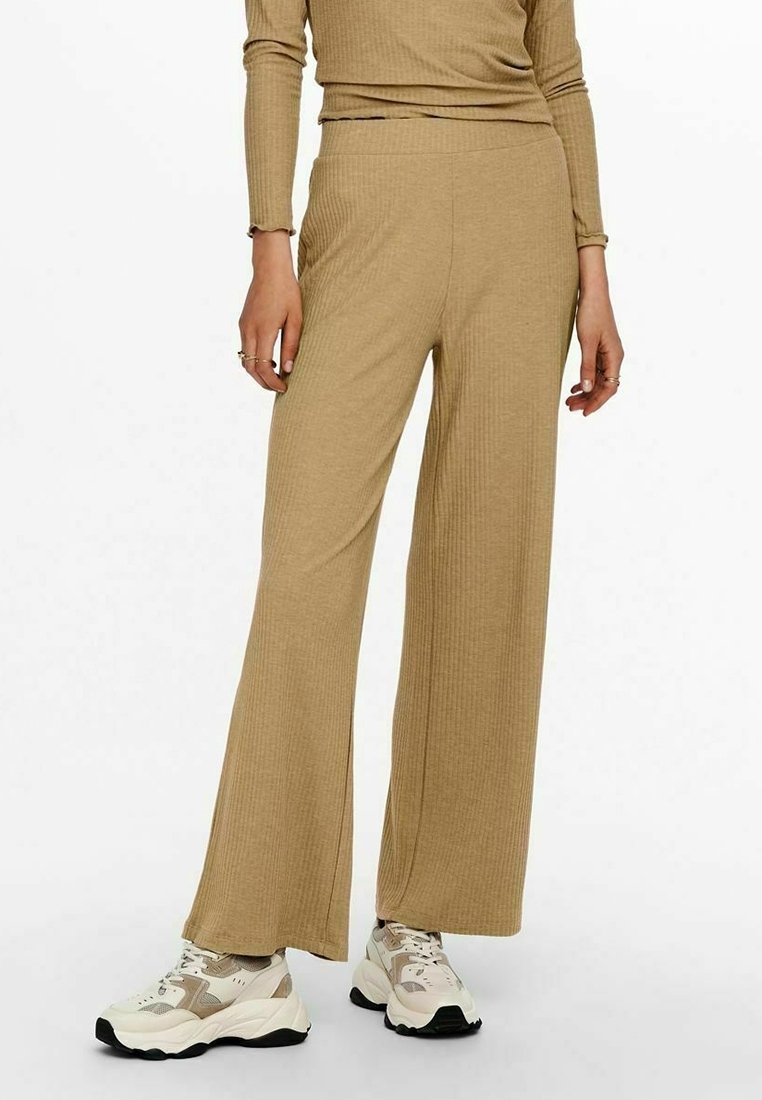 Femme portant un pantalon large beige côtelé et un haut à manches longues assorti, associé à des baskets épaisses blanches et beiges.