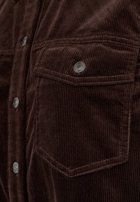 Brun manchesterkjorta med texturerad yta, vertikal ränder, två bröstfickor och metallknappar.