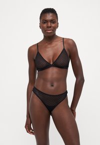 Svart undertøysett som inkluderer en gjennomsiktig, prikket trekant-bralette og matchende høytlivstanga, laget av lett mesh-stoff.