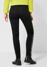 Mustat leggingsit kapealla leikkauksella, joissa on neonkeltaiset sivuraidat ja takataskut, yhdistettyinä mustiin nilkkureihin.