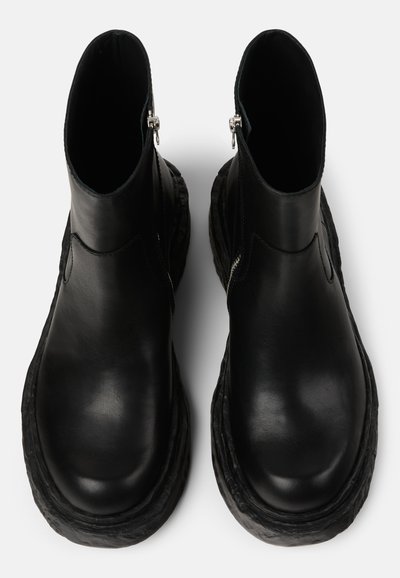 Botas de tobillo de cuero negro con un diseño elegante, suela de goma texturizada y acentos de cremallera plateada en el costado. Superficie suave y punta redondeada.