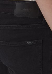 Área del bolsillo trasero de unos jeans de mezclilla negros de Marc O’Polo con parche de cuero de la marca y etiqueta de tela visibles.