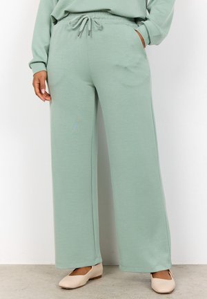 Pantaloni larghi verde chiaro realizzati in tessuto morbido. Presentano una vita elastica con cordino e tasche laterali. Cuciture piatte e una vestibilità rilassata.