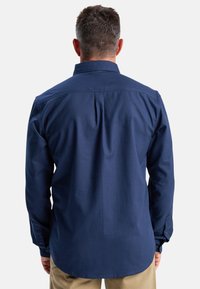 Navy blouse met lange mouwen, achterkant met plooi en afgeronde zoom. De stof lijkt glad en lichtgewicht, met een klassieke kraagontwerp.