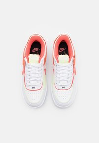 Vita atletiska skor med en smidig läderövre del, neon gula detaljer, klara korallöverlägg och perforeringar på tån.