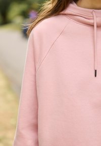 Felpa in cotone rosa con cappuccio, caratterizzata da una vestibilità comoda e maniche raglan. La texture è morbida con una finitura liscia e delicata.