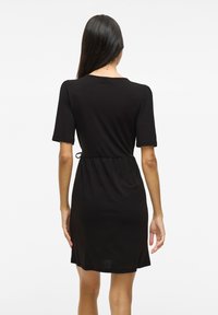 Μαύρο φόρεμα κοντό μανίκι με χαλαρή εφαρμογή, που διαθέτει κορδόνι στη μέση για ρυθμιζόμενο μέγεθος και λεία, ελαφριά ύφανση.