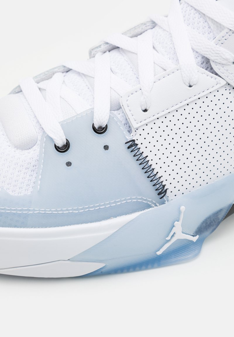 Sneaker blanche avec une tige en mesh et en cuir, dotée d'une semelle bleue translucide, d'accents perforés, et de coutures noires avec un logo Jordan.
