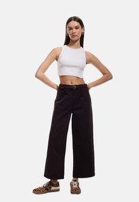 Top corto blanco, pantalones de pierna ancha negros con detalle de cinturón marrón y zapatillas marrones con patrón de leopardo. Diseño simple, ajustado y casual.