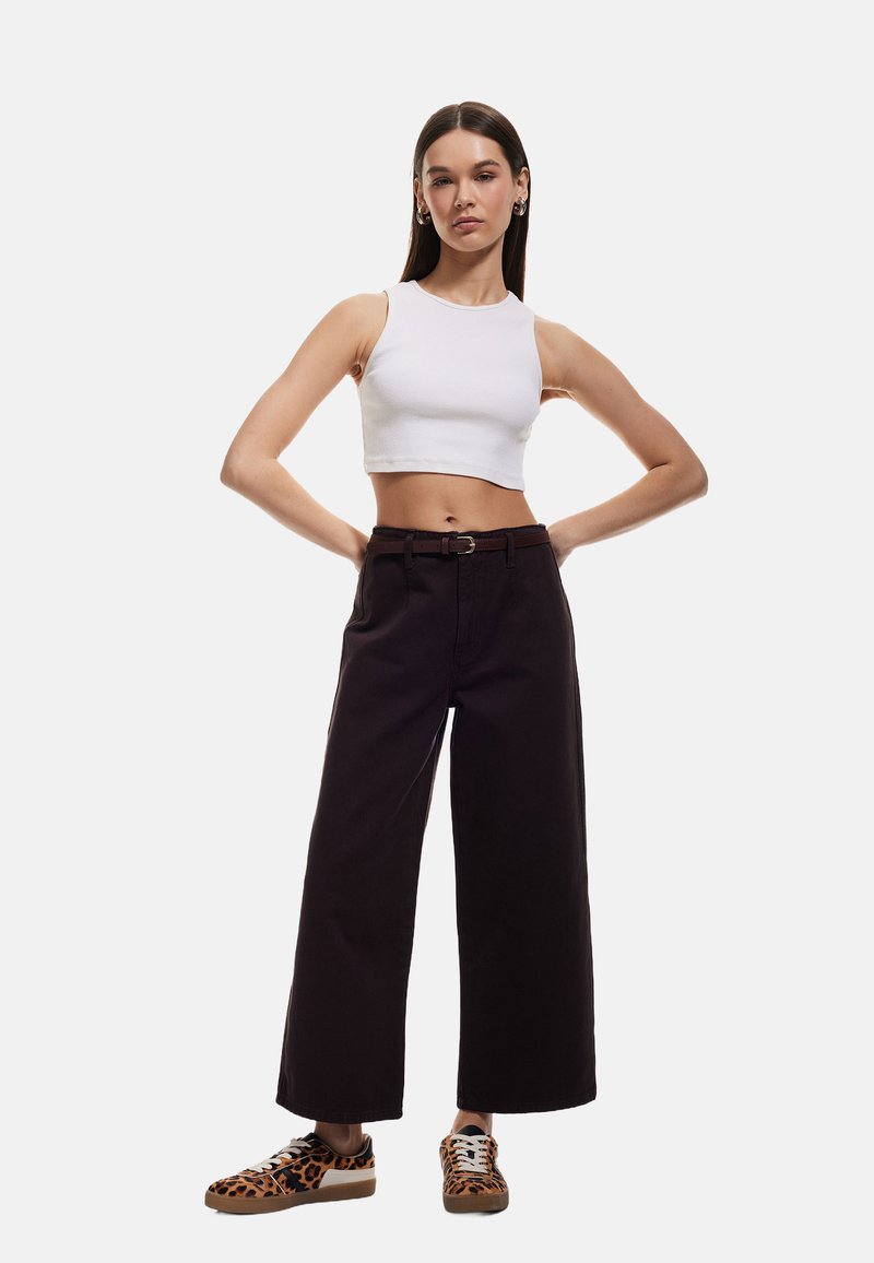 Top corto blanco, pantalones de pierna ancha negros con detalle de cinturón marrón y zapatillas marrones con patrón de leopardo. Diseño simple, ajustado y casual.