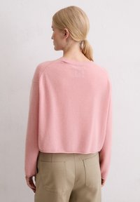 Pull en cachemire rose court avec un col rond, des bords côtes et une texture douce. Porté avec un pantalon taille haute kaki.