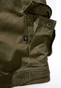 Material de culoare verde măsliniu, cu o textură netedă, având un buton și un eticheta logo vizibil. Include o buzunar cu clapetă și detalii de cusătură.
