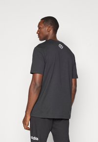 Juoda trumpa rankovėmis marškinėliai su apvalia iškirpte, ant nugaros turi mažą baltą geometrinį logotipą. Pagaminta iš minkštos, kvėpuojančios medžiagos.