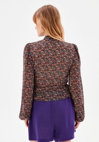 Bluse med blomsterprint og lange ærmer, mørk baggrund og farverige blomster. Har puffede skuldre og rundet kant.