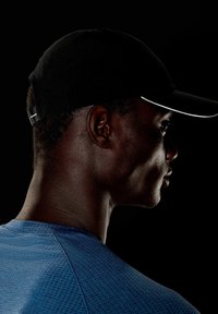 Schwarze Kappe mit gebogenem Schild, verfügt über einen weißen Akzent, getragen mit einem strukturierten blauen Sportshirt. Seitenansicht vor einem dunklen Hintergrund.