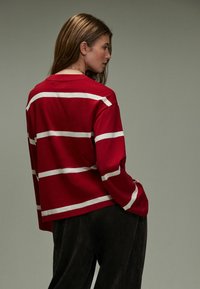 Rotes Langarmhemd mit weißen horizontalen Streifen, aus weichem Stoff, kombiniert mit dunklen Cordhosen in legerem Schnitt.