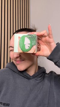 Confezione verde con coperchio trasparente che mostra tamponi di cotone bianchi all'interno. Scatola aperta sopra, tenuta da una persona con felpa grigia con cappuccio.