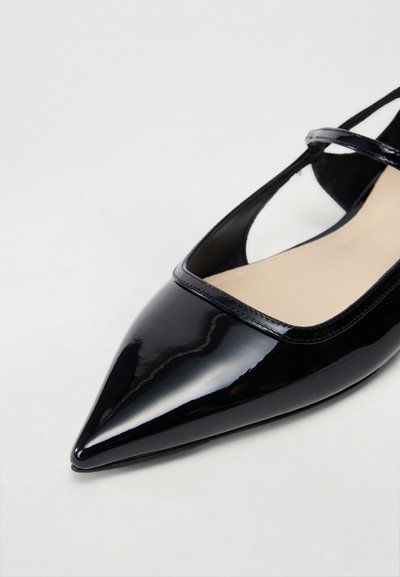 Μαύρο παπούτσι στιλέτο από γυαλιστερό δέρμα με μυτερή μύτη και κομμένες πλευρές, διαθέτει λεπτή λωρίδα γύρω από τον αστράγαλο και μπεζ σόλα.