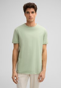 Helles grünes T-Shirt mit kurzen Ärmeln aus weicher Baumwolle, mit rundem Ausschnitt und geradem Saum, der eine leichte Textur aufweist.