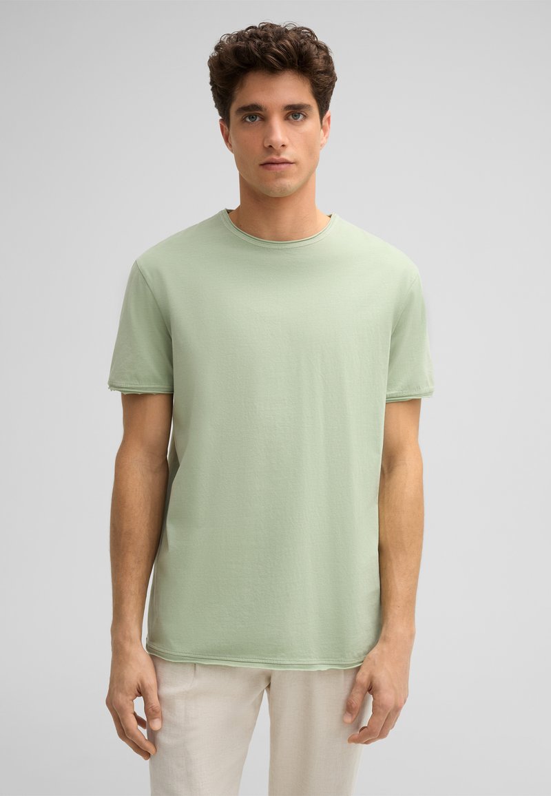 Helles grünes T-Shirt mit kurzen Ärmeln aus weicher Baumwolle, mit rundem Ausschnitt und geradem Saum, der eine leichte Textur aufweist.