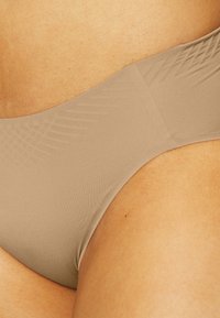 Nude bikini bottom in soft, stretchy material. Features a smooth texture with a wide waistband and minimal coverage design.