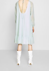 Robe vert clair avec un décolleté plongeant, des manches longues transparentes et un ourlet froncé. Portée avec des bottes blanches brillantes jusqu'au genou.