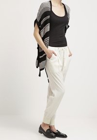 Cardigan de style kimono à rayures noires et blanches, porté sur un débardeur noir, associé à un pantalon clair et des mocassins noirs.