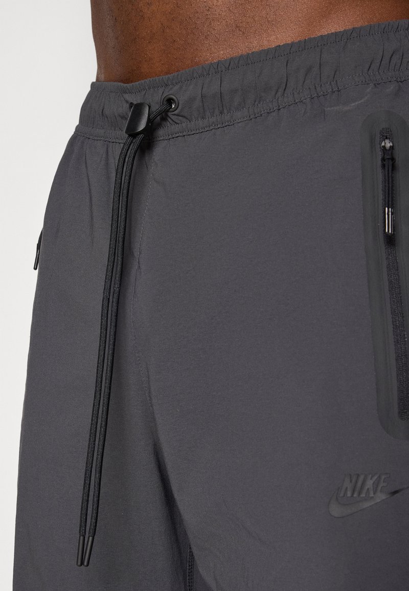 Szare spodenki sportowe z elastyczną talią i sznurkiem do regulacji. Posiadają kieszenie na zamek i logo Nike po boku. Gładka faktura materiału.