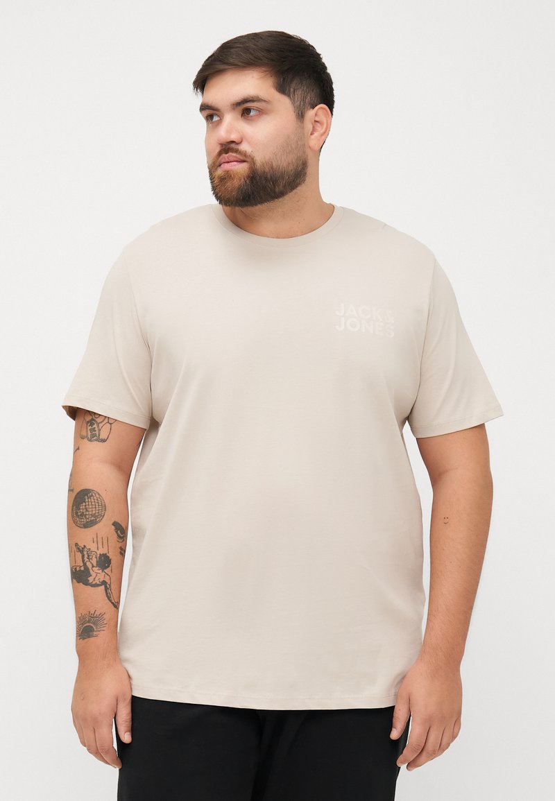 Beige T-shirt met korte mouwen en een ronde hals, met een klein wit logo op de linkerkant van de borst, gemaakt van een gladde, rekbare stof.