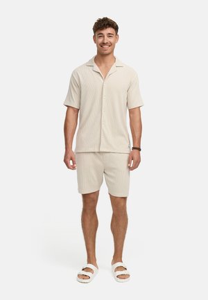 Light beige short-sleeve button-up shirt and matching shorts made of textured fabric; worn with white slip-on sandals.
