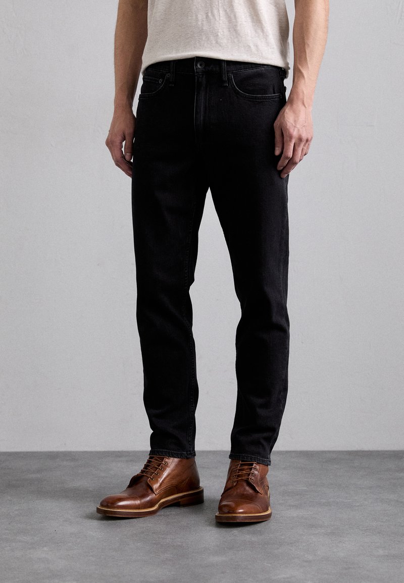 Jeans de mezclilla negra con un corte ajustado, cinco bolsillos y una cintura clásica, combinados con botas de cuero marrón con cordones.