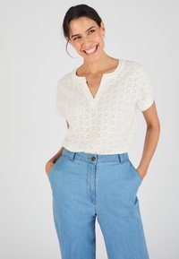 Witte top met korte mouwen en een gestructureerd patroon, met een V-hals. Draag het met lichtblauwe wijde jeans met voorzakken.