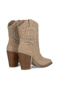 Botines de ante beige con un tacón marrón apilado, adornados con remaches plateados y azules en un patrón decorativo a lo largo del caña.