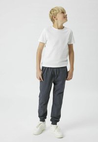 Weißes Baumwoll-T-Shirt kombiniert mit dunkelgrauen Jogginghosen, die einen elastischen Bund und zulaufende Bündchen haben. Weiße Sneaker runden das Outfit ab.