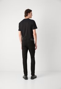 Camiseta de algodón negra de manga corta, combinada con jeans negros ajustados que tienen un parche de cuero en la parte posterior y un diseño minimalista.