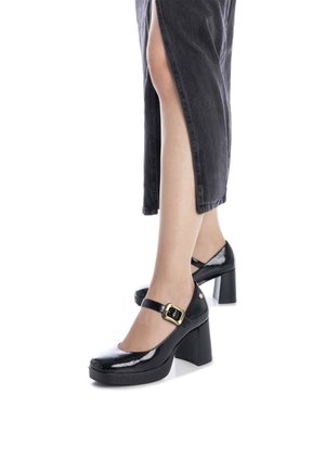 Zapatos Mary Jane de charol negro con punta redonda, correa al tobillo con un hebilla dorada y un tacón alto y grueso.