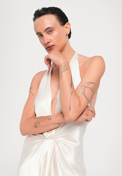 Satinová halter šaty v krémovej farbe, s hlbokým V-výstrihom, opleteným uzlom v páse a hladkou, lesklou textúrou.