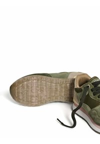 Pair of olive green and beige sneakers, one shoe showing textured sole with logo, the other showing laces and padded collar on white background.