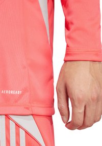 Roze sportshirt met een gladde textuur, lange mouwen en een witte accent aan de zijkant. Bevat 'AEROREADY' branding vlakbij de zoom.