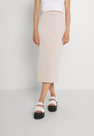 Beżowa midi spódnica z tkaniny z elastyczną talią, zestawiona z białymi sandałami na platformie z miękkimi paskami i czarną podeszwą.