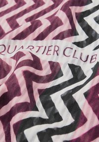 Patroon in textiel met zigzagontwerpen in tinten roze, zwart en wit, met het 'Quartier Club'-logo geïntegreerd in het ontwerp.