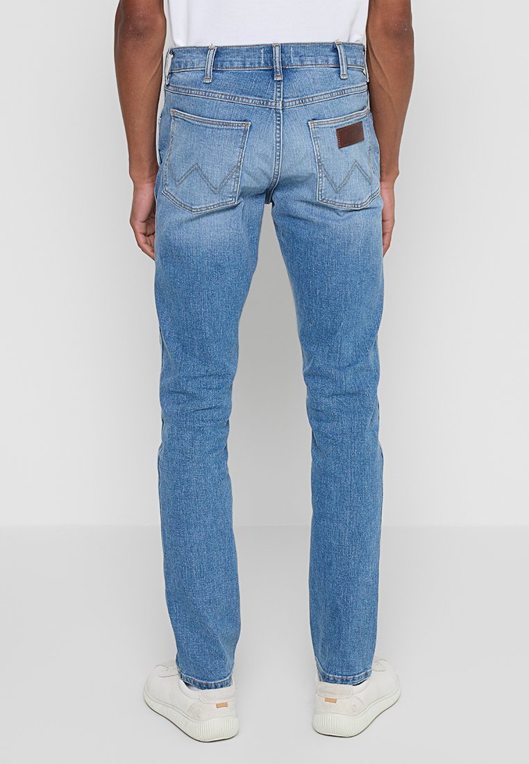 Jasnoniebieskie dżinsy o slim fit, z dwoma ukośnymi tylnymi kieszeniami i brązową skórzaną naszywką na pasku.