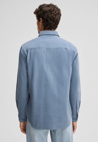 Lichtblauwe lange mouwen shirt van zachte stof. Heeft een kraag, knoopmanchetten en een rechte zoom. Eenvoudig, modern ontwerp.