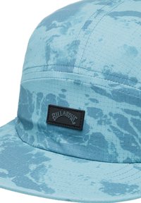 Cappello blu con un motivo tie-dye testurizzato. Presenta un patch di marca nero sul davanti e una visiera rigida e ampia. Realizzato in tessuto leggero.