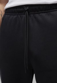 Černé tepláky s elastickým pasem a nastavitelným šňůrkovým páskem. Hladká textura látky s jemnými švovými detaily.